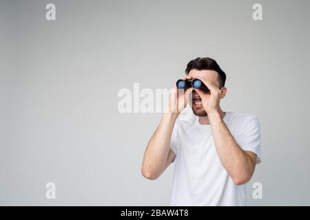 Giovane uomo isolato sullo sfondo. Guy guardare binocolo lontano. Afferrare con entrambe le mani ed esaminare. Spia o ragazzo dall'aspetto informale. Foto Stock