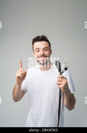 Giovane uomo isolato sullo sfondo. Ragazzo con presa e cavo in mani che puntano su di esso e sorridere sulla fotocamera. Immagine del giovane maestro pronto per la riparazione Foto Stock