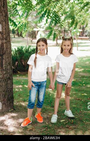 Due ragazze in t-shirt bianche stanno tenendo le mani nel parco all'aperto. Simulazione. Foto Stock