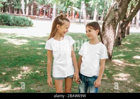 Due ragazze piccole in magliette bianche che si trovano nel parco all'aperto. Simulazione. Foto Stock