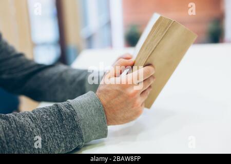 Giovane uomo che legge il vecchio libro di carta aperto al tavolo, primo piano, stile vintage Foto Stock