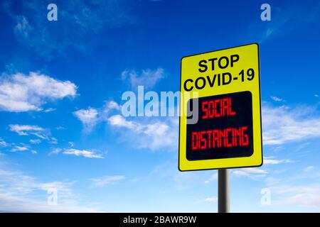 Un segno Stop COVID-19 con un messaggio digitale luminoso sulle distanzazioni sociali e con spazio di copia contro il cielo blu. Concetto di prevenzione della diffusione del c Foto Stock