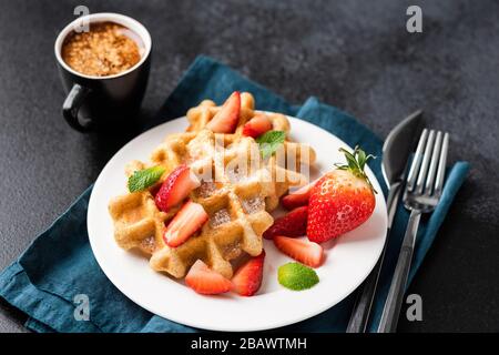 Gustosi waffle belgi con fragole e una tazza di caffè espresso su sfondo nero Foto Stock