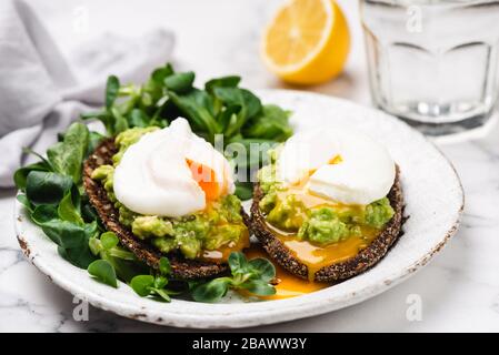 Pane tostato di segale avocado con uova in camicia sul piatto. Antipasti sani, colazione, pranzo o spuntino. Tuorlo d'uovo runny Foto Stock