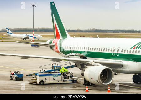 BUDAPEST, UNGHERIA - MARZO 2019: Airbus A320 Jet gestito da Alitalia all'aeroporto di Budapest. La porta di carico è aperta e il carrello del caricatore bagagli è parcheggiato Foto Stock