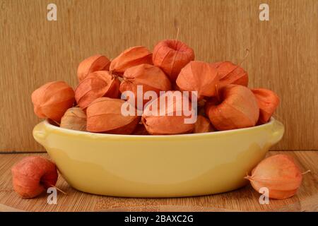 Physalis rosso commestibile in vaso di ceramica gialla su sfondo di legno Foto Stock