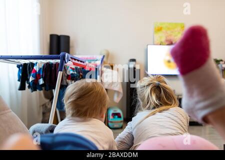 Vista posteriore di due carino piccolo caucasico ragazzo e ragazza sdraiato su divano guardare cartoni animati o film su tv set con servizio di streaming. Soggiorno per bambini Foto Stock