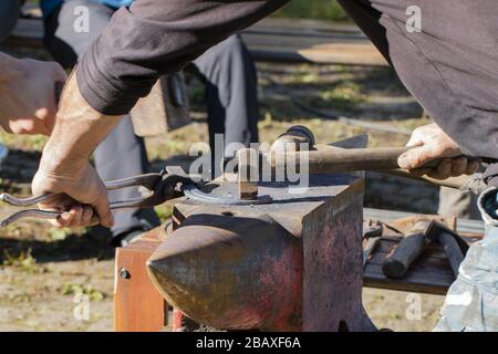 Fabbro forgiando un ferro di cavallo con utensili tradizionali: Incudine, martello e pinze Foto Stock