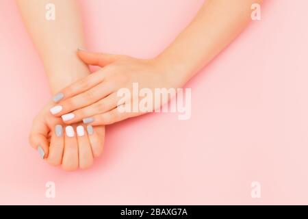 Manicure femminile alla moda. Bella mano della giovane donna con manicure perfetta su sfondo rosa. Stile a disposizione piatta. Foto Stock