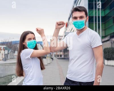 Urto del gomito. Due persone donna, uomo che indossa maschera medica, gli amici si salutano con i gomiti, invece di scuotere le mani guardando la fotocamera che mostra la n Foto Stock