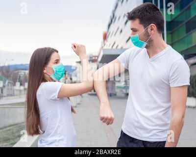 Due persone donna e uomo che indossano maschera medica, gli amici si salutano con i gomiti, invece di scuotere le mani. Urto del gomito. Un nuovo modo di saluto Foto Stock