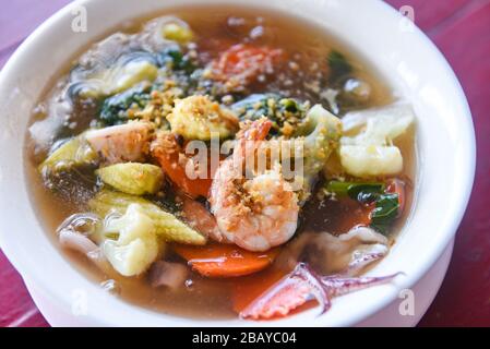 Tagliatelle di pesce con salsa spessa con gamberi calamari gamberi gamberi e verdure su ciotola su sfondo tavola di legno Foto Stock