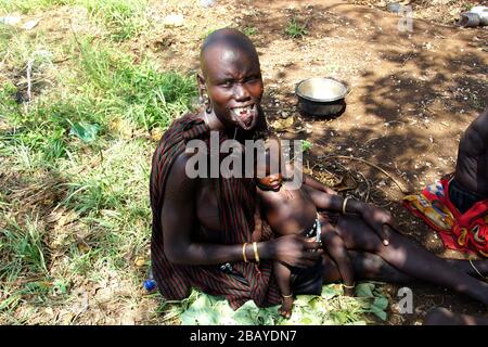 Mursi Tribe Mum senza labbro piastra culla il suo bambino nel suo giro Foto Stock