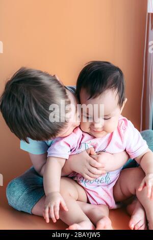 felice fratellino giocando abbraccia il suo bambino sorella, ragazzo e ragazza abbraccia baci, concetto di amore e parenting Foto Stock