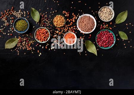 Assortimento di legumi, sparato dalla parte superiore su uno sfondo nero con un luogo per il testo. Lenticchie, fagioli di soia, ceci, fagioli rossi, vellutata di legumi Foto Stock