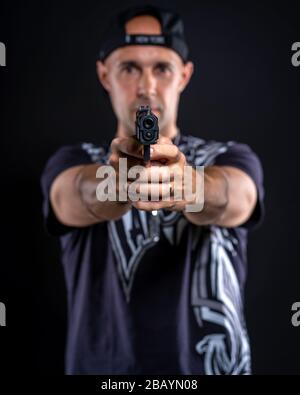 uomo che punta la pistola a oggetti, ritratto su sfondo nero Foto Stock