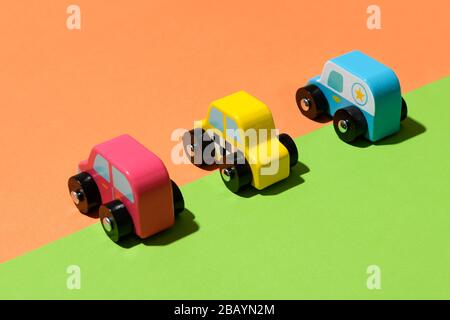 Tre colorate auto giocattolo rustiche in legno artigianale su uno sfondo verde e arancione diviso allineato lungo la diagonale divisione di colore Foto Stock