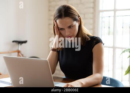 Donna d'affari che siede alla scrivania che legge sul laptop messaggio sgradevole Foto Stock