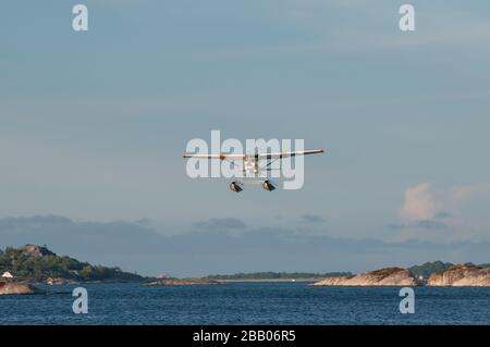 Un idrovolante giallo e bianco Cessna 172 Skyhawk che parte tra le isole dell'arcipelago di Kragerø sulla costa meridionale della Norvegia. Foto Stock