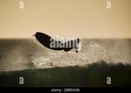 Un surfista solista che cattura le onde nell'Oceano Atlantico alla spiaggia di Llandudno sulla costa occidentale silhouette dal sole che tramonta. Foto Stock