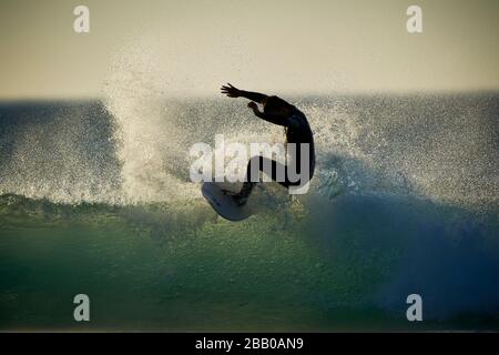 Un surfista solista che cattura le onde nell'Oceano Atlantico alla spiaggia di Llandudno sulla costa occidentale silhouette dal sole che tramonta. Foto Stock