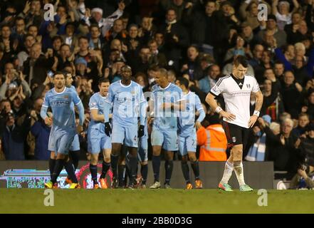 John Arne Riise di Fulham appare sconsolato dopo che Jesus Navas (oscurato) della città di Manchester ha segnato il terzo gol della sua squadra e celebra con i compagni di squadra Foto Stock