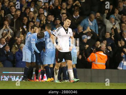 John Arne Riise di Fulham appare sconsolato dopo che Jesus Navas (oscurato) della città di Manchester ha segnato il terzo gol della sua squadra e celebra con i compagni di squadra Foto Stock