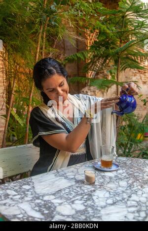 Fes, Marocco: Giovane donna che versa il tè in un giardino Foto Stock