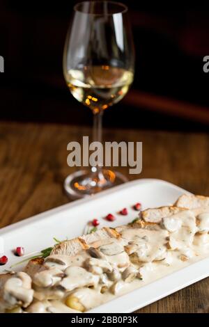 Carne di pollo su gnocchi grattugiati in salsa di funghi e formaggio affumicato in tavola con bicchiere di vino bianco Foto Stock
