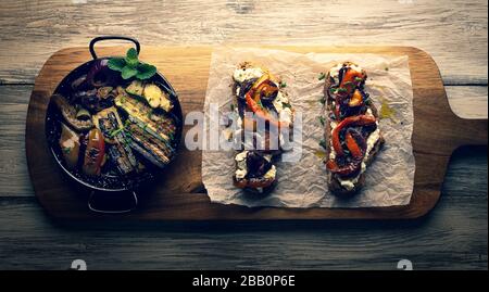 Fette di pane rustiche su una vecchia tavola di legno con verdure grigliate ed erbe, stile vintage e retrò, colori luminosi, piatto vegetariano, Vista dall'alto, piatto Foto Stock