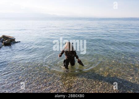 Female Scuba Diving Instructor in piedi in acqua indossando un Dry Suit, un Twin Tank e pinne di tenuta Foto Stock