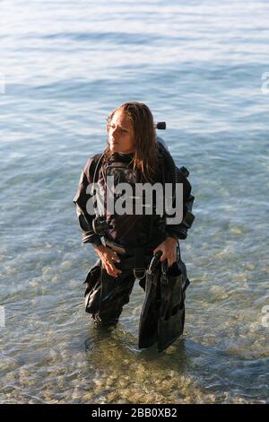 Female Scuba Diving Instructor in piedi in acqua indossando un Dry Suit, un Twin Tank e pinne di tenuta Foto Stock