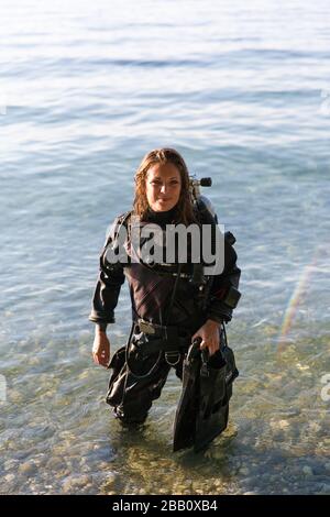 Female Scuba Diving Instructor in piedi in acqua indossando un Dry Suit, un Twin Tank e pinne di tenuta Foto Stock