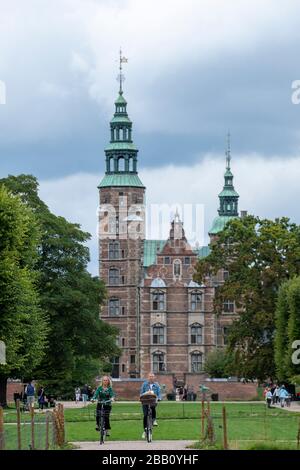 Due ciclisti che fanno il loro giro in bicicletta davanti al Castello di Rosenborg a Copenhagen, Danimarca, Europa Foto Stock