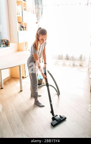 Ragazza adolescente che pulisce la sua stanza con aspirapolvere. La comodità dei bambini e le pulizie aiutano a concepire il concetto Foto Stock