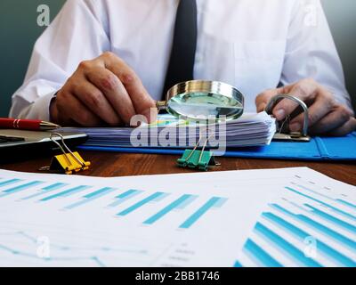 Auditor effettua un audit interno della società e controlla la relazione finanziaria con lente d'ingrandimento. Foto Stock