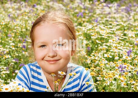 Ragazza carina su un campo di fioritura di margherite in una giornata estiva soleggiata. Primo piano ritratto di un bambino. Foto Stock