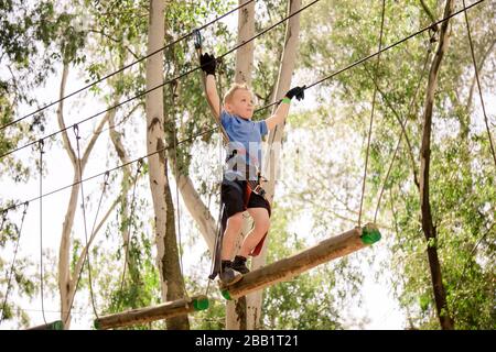 Foto a colori di un giovane bel ragazzo che sale su funi sospese o cavi in un parco all'aperto. Nota anche come zipline via cavo. Foto Stock