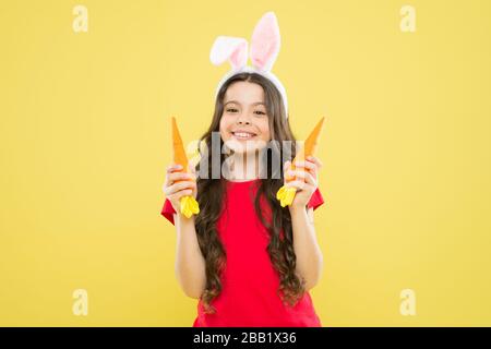 Le vacanze di Pasqua stanno arrivando. Cibo sano. Orecchie di coniglio bambino. Dieta per la salute. Benefici di mangiare la carota. Carota di Pasqua. Ragazza tenere carota. Gioca con il cibo. Tradizione primaverile. Sfondo giallo bambino. Foto Stock