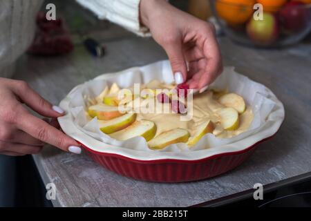 La padrona di casa sta preparando la mela charlotte in cucina. Mette il bacche su una torta di mele in un piatto da forno. Pasta di mele cruda Foto Stock