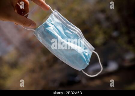 Profondità poco profonda dell'immagine del campo (fuoco selettivo) con la mano di un uomo che tiene una maschera medica del naso e della bocca. Foto Stock