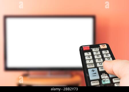 Uomo caucasico che guarda la TV a casa con schermo bianco. Modifica dei canali e regolazione del volume con il telecomando del televisore. Foto Stock