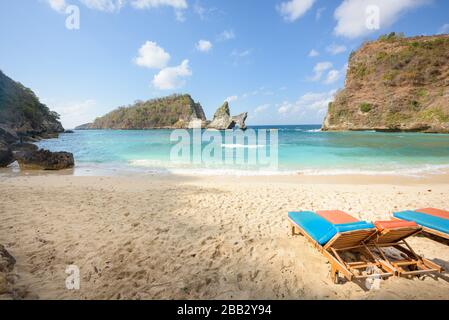 Popolare luogo di foto e destinazione turistica Atuh Beach. Sedie a sdraio vuote su una spiaggia di sabbia tropicale, con rocce di mare e scogliere in lontananza, e tu Foto Stock