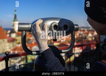 Uomo in guanti di lattice guardando attraverso il binocolo turistico al punto panoramico nella città vecchia di Tallinn, Estonia Foto Stock