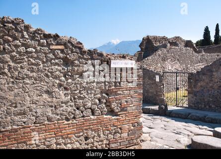 Antica strada e case in rovina nell'antica città di Pompei, Italia. La vetta del Vesuvio si può vedere sullo sfondo. Foto Stock