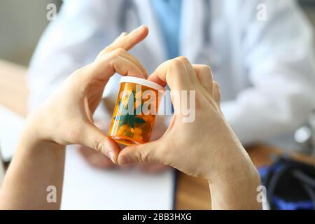 Le mani che tengono le capsule nel vaso con il segno della marijuana Foto Stock