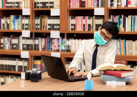 Lavoro superlavorato multitasking uomo mentre parla sul cellulare, utilizzando il laptop. Lavorare da casa indossando la maschera protettiva. Pulendo le mani con Foto Stock