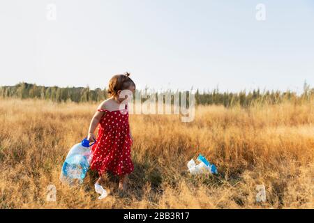 La bambina raccoglie i rifiuti sparsi nella foresta. La bambina raccoglie i rifiuti sparsi nella foresta. Il bambino lotta per un ambiente pulito. Foto Stock