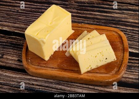 Piatto di burro di legno con un pezzo di burro e fette di formaggio su un fondo di legno. Primo piano Foto Stock