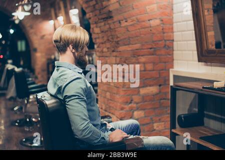 Barbershop concetto. Ritratto posteriore di uomo duro barbuto. Ha un'acconciatura alla moda, un taglio di capelli moderno, che indossa jeans casual vestito Foto Stock